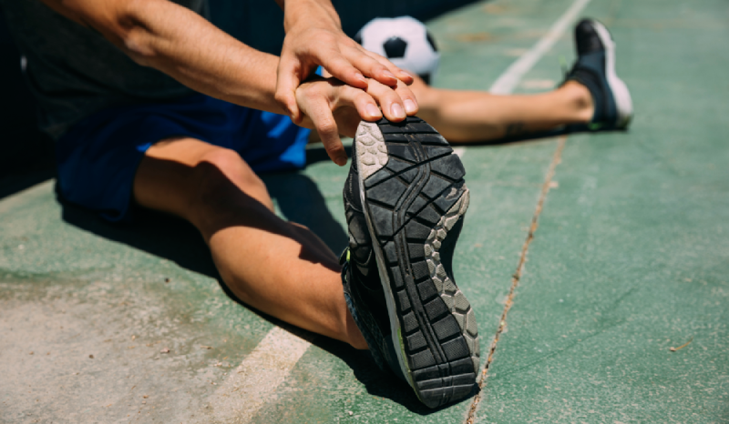 Close up de uma pessoa alongando a perna em um campo de concreto verde. Imagem ilustrativa para representar o tema de direito desportivo.